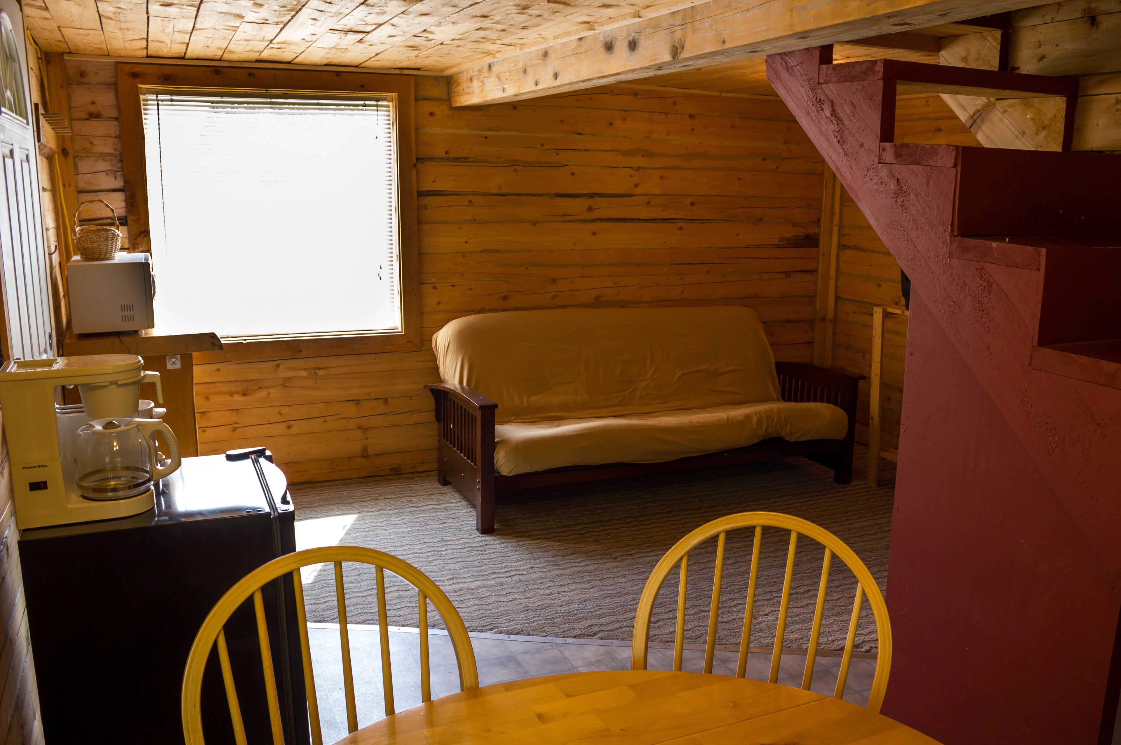 Una cabaña acogedora con interior de madera, una cama, una cafetera y una mesa de comedor con sillas.