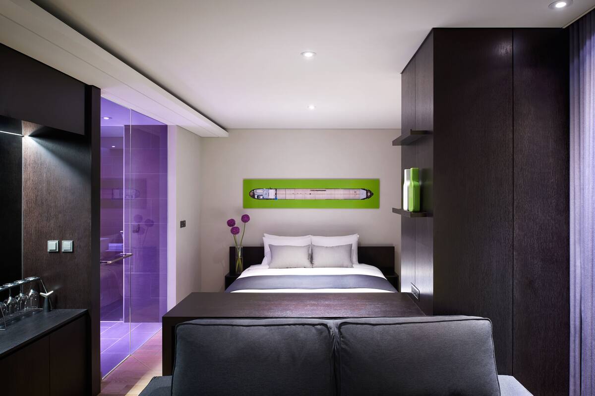 Une chambre moderne avec un grand lit, une table de chevet, une commode et une salle de bain dotée d’une douche en verre.