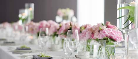 A long dining table with clear glassware, pink flowers, and candles.