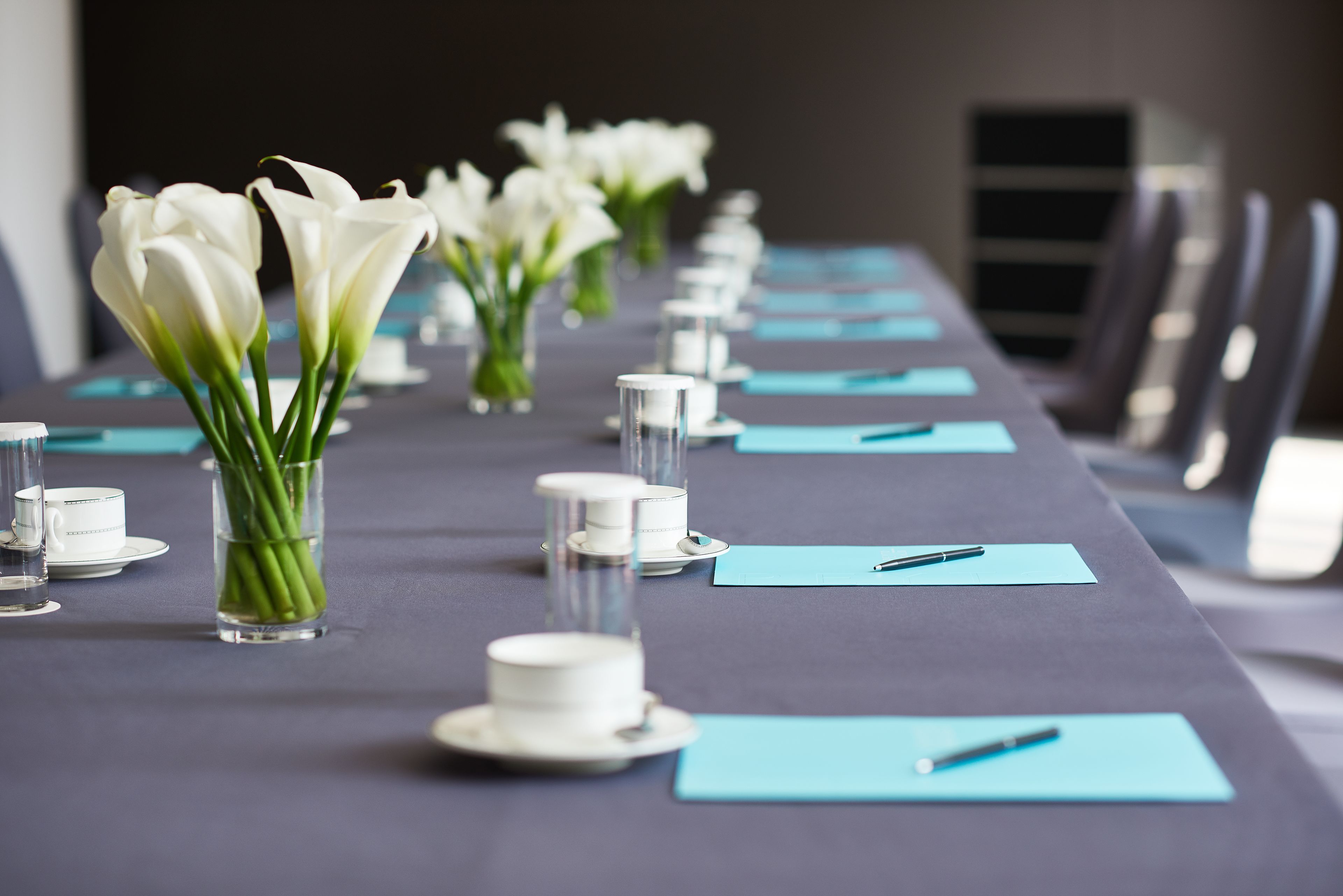 Una mesa de conferencias con jarrones de flores blancas, cristalería transparente y servilletas azules.