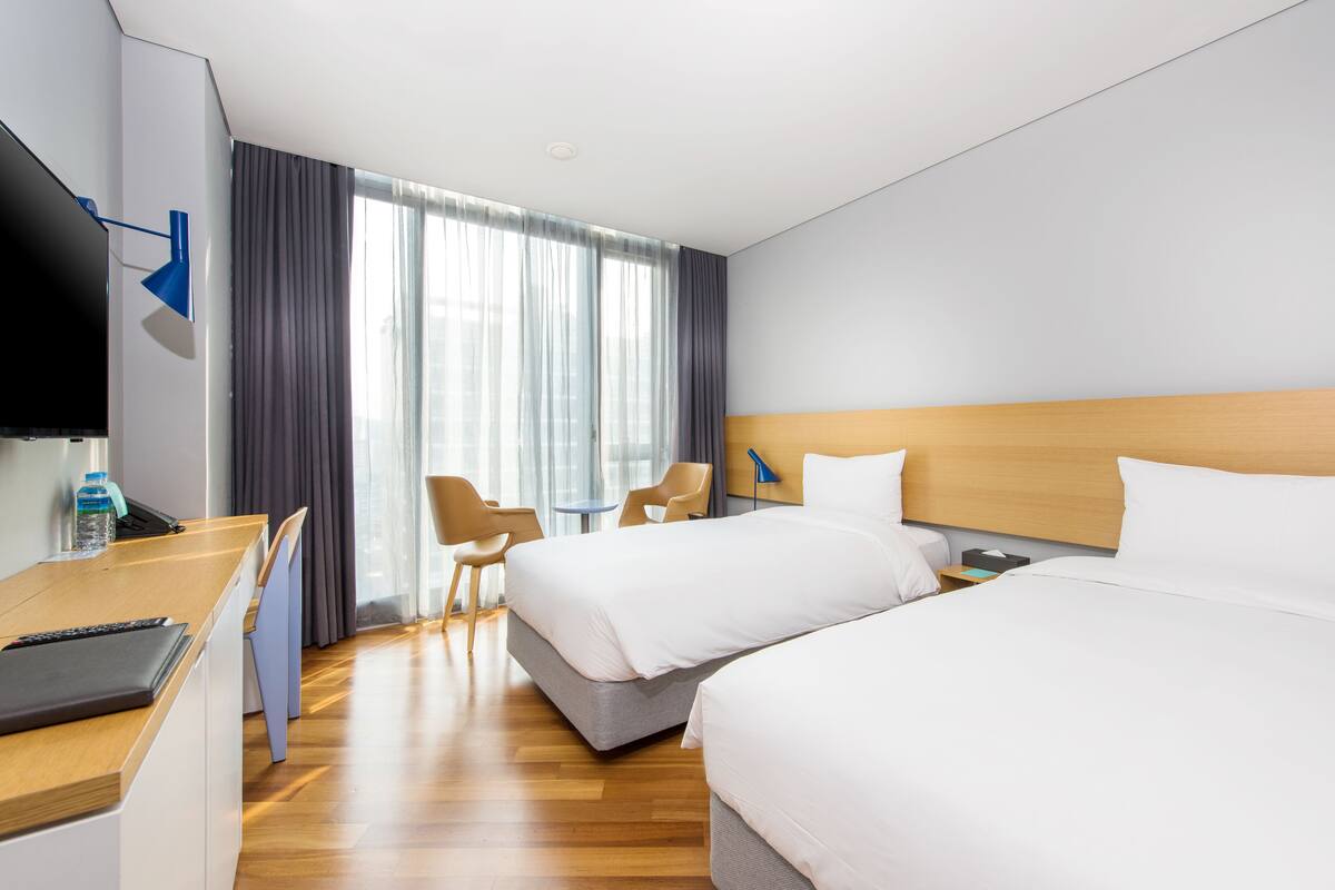 Une chambre d’hôtel avec deux lits, un bureau avec un ordinateur portable, une télévision et une fenêtre avec des rideaux.