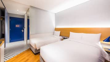 A modern hotel room with two beds, a wooden headboard, a small bedside table, and a blue door.