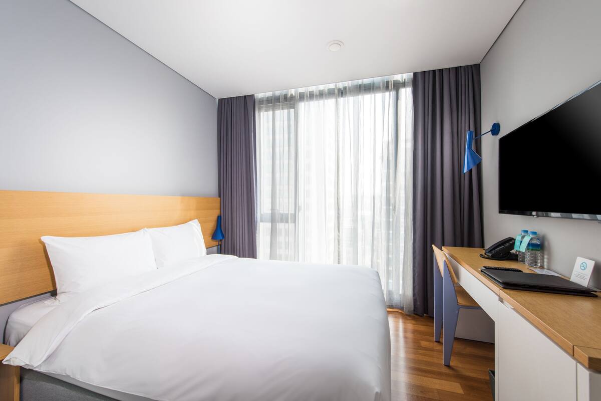 Une chambre d’hôtel équipée d’un lit, d’un bureau avec un ordinateur portable, d’un téléphone et d’une télévision.