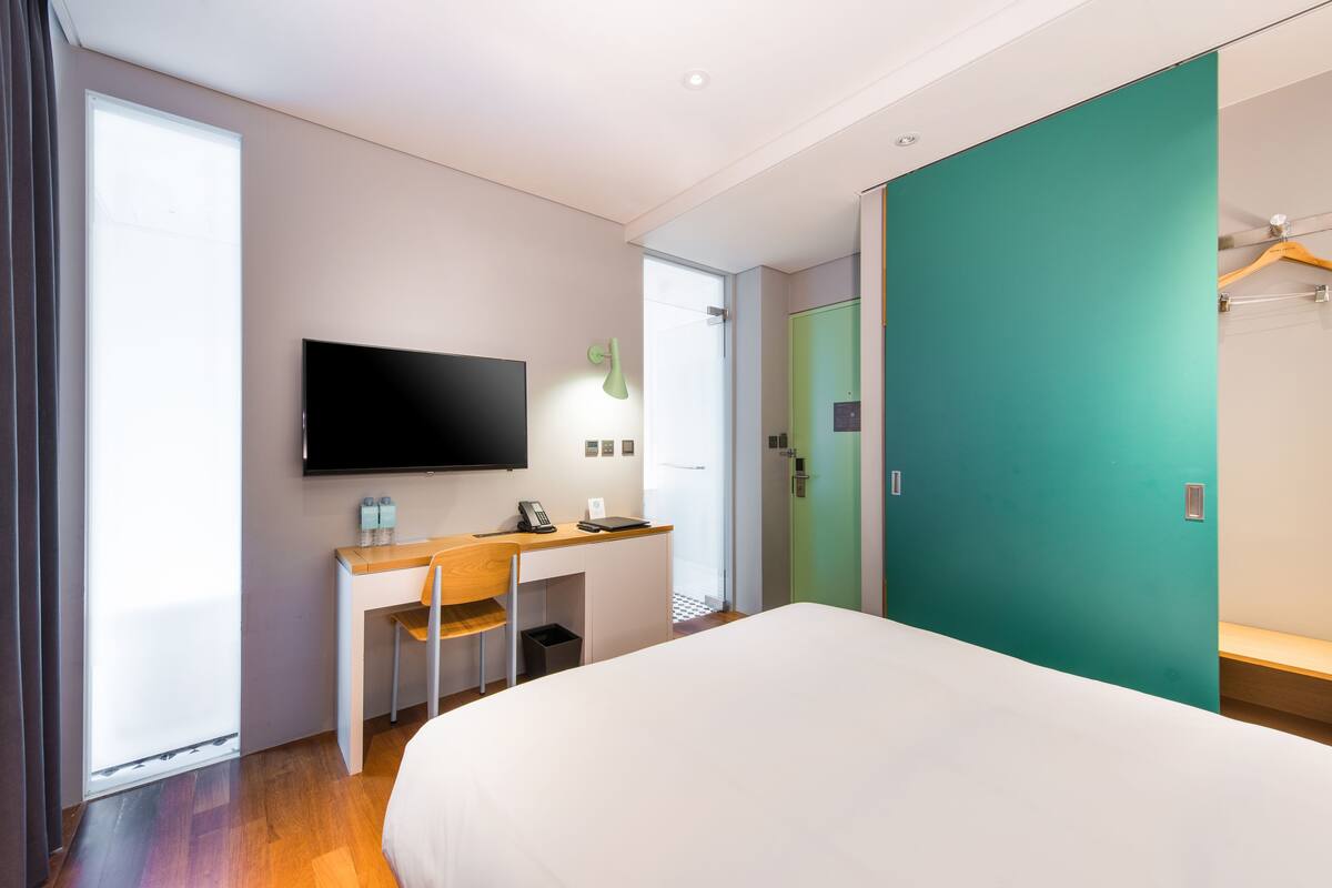 Une chambre d’hôtel moderne dotée d’un grand lit, d’un bureau avec une chaise, d’un téléviseur à écran plat et d’un mur vert.