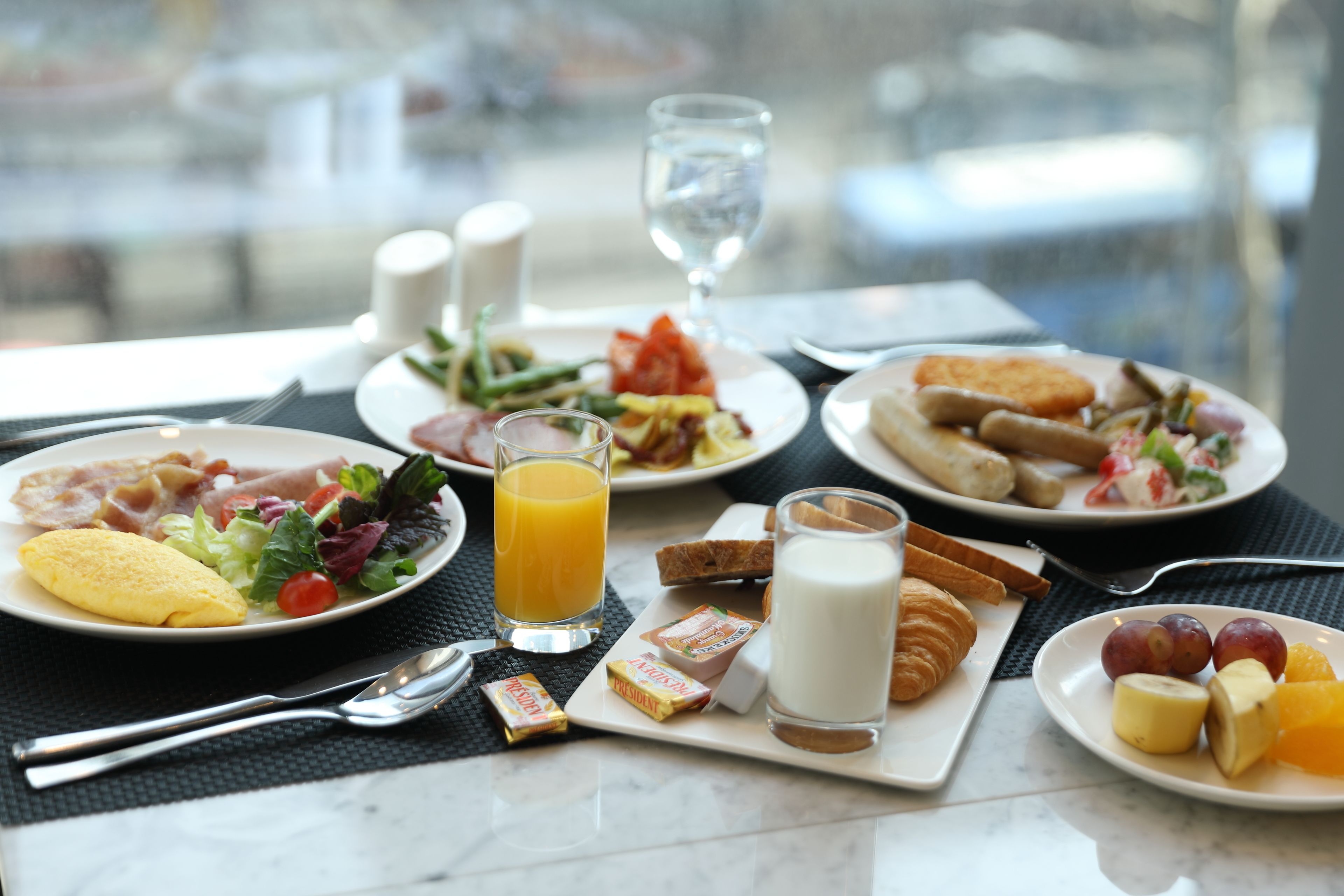 A breakfast setting with plates of food, including eggs, toast, and fruit, along with a glass of orange juice and a glass of milk.