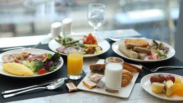 A breakfast setting with plates of food, including eggs, toast, and fruit, along with a glass of orange juice and a glass of milk.