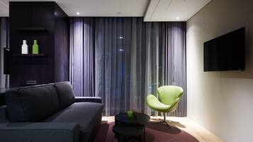 A modern living room with a grey sofa, a green chair, a small black table, and a TV mounted on the wall.