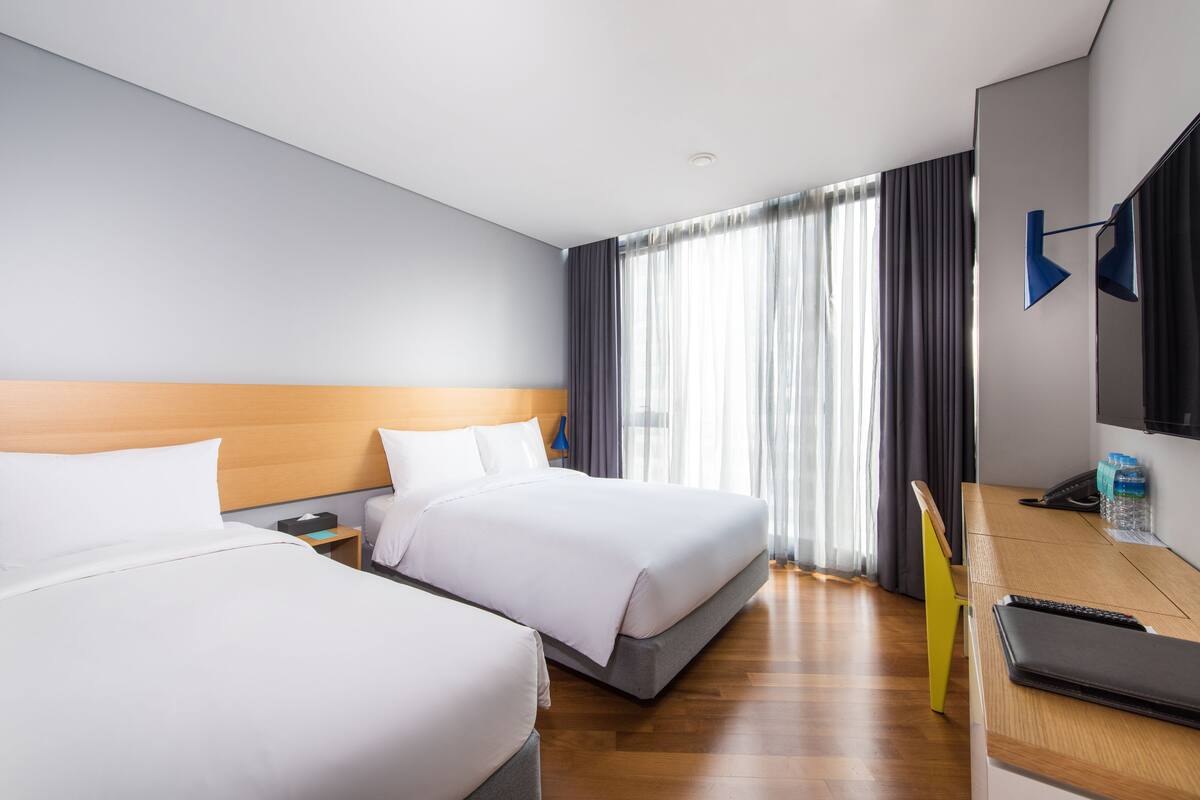 Une chambre d’hôtel avec deux lits, un bureau, une chaise, une télévision et une fenêtre avec des rideaux.