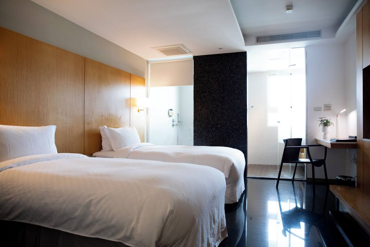 A hotel room with two beds, a desk, a chair, and a large window.