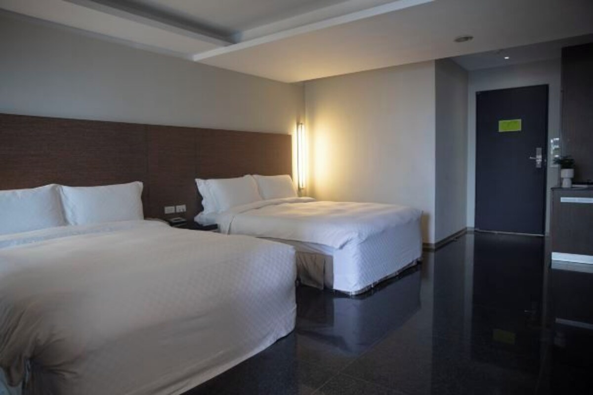 Een hotelkamer met twee bedden, een nachtkastje, een wandlamp en een deur met een bordje.