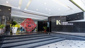Une entrée moderne, marquée par un grand panneau en forme de « K », une structure décorative rouge et un escalier menant à l’entrée.