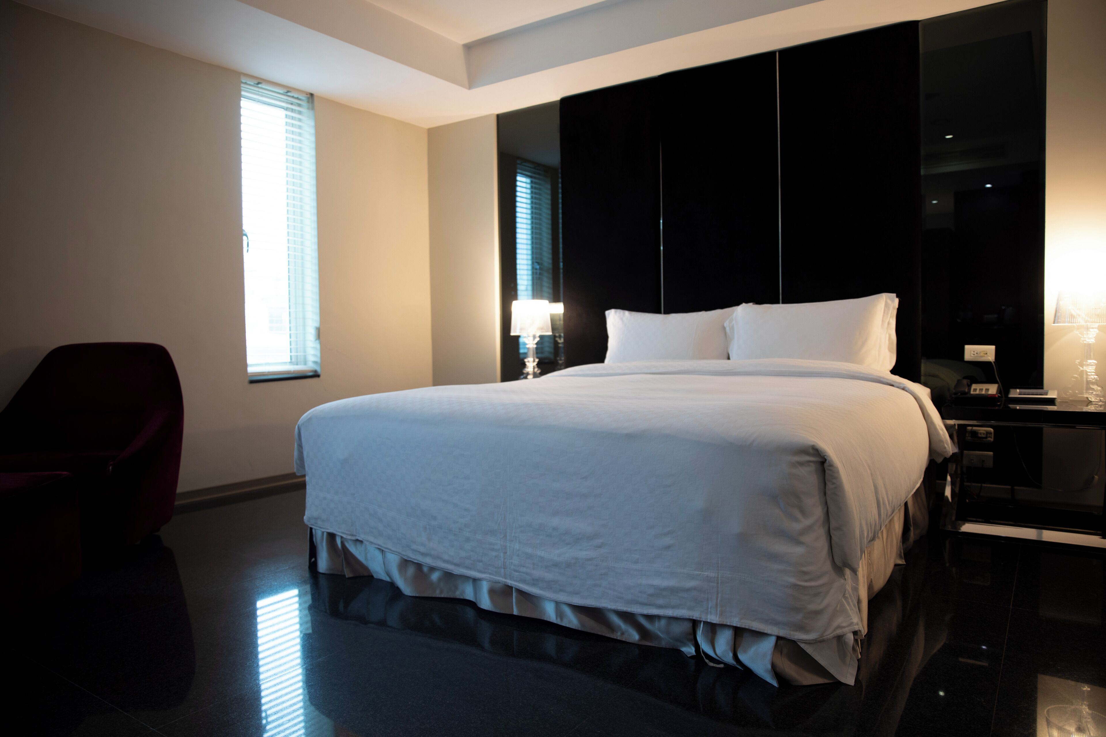 Una habitación de hotel moderna con una cama grande, una silla roja y un espejo amplio.