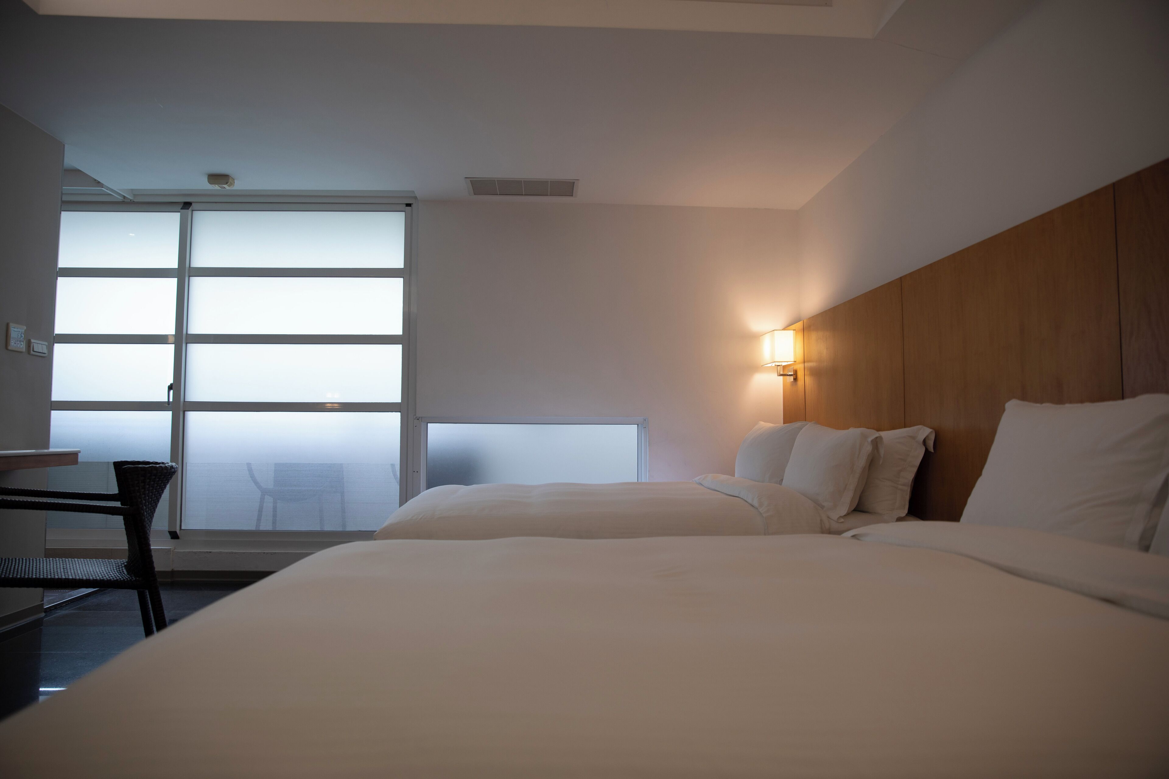 A hotel room with a large bed, a desk, and a chair. There is a window with a view of the outside.