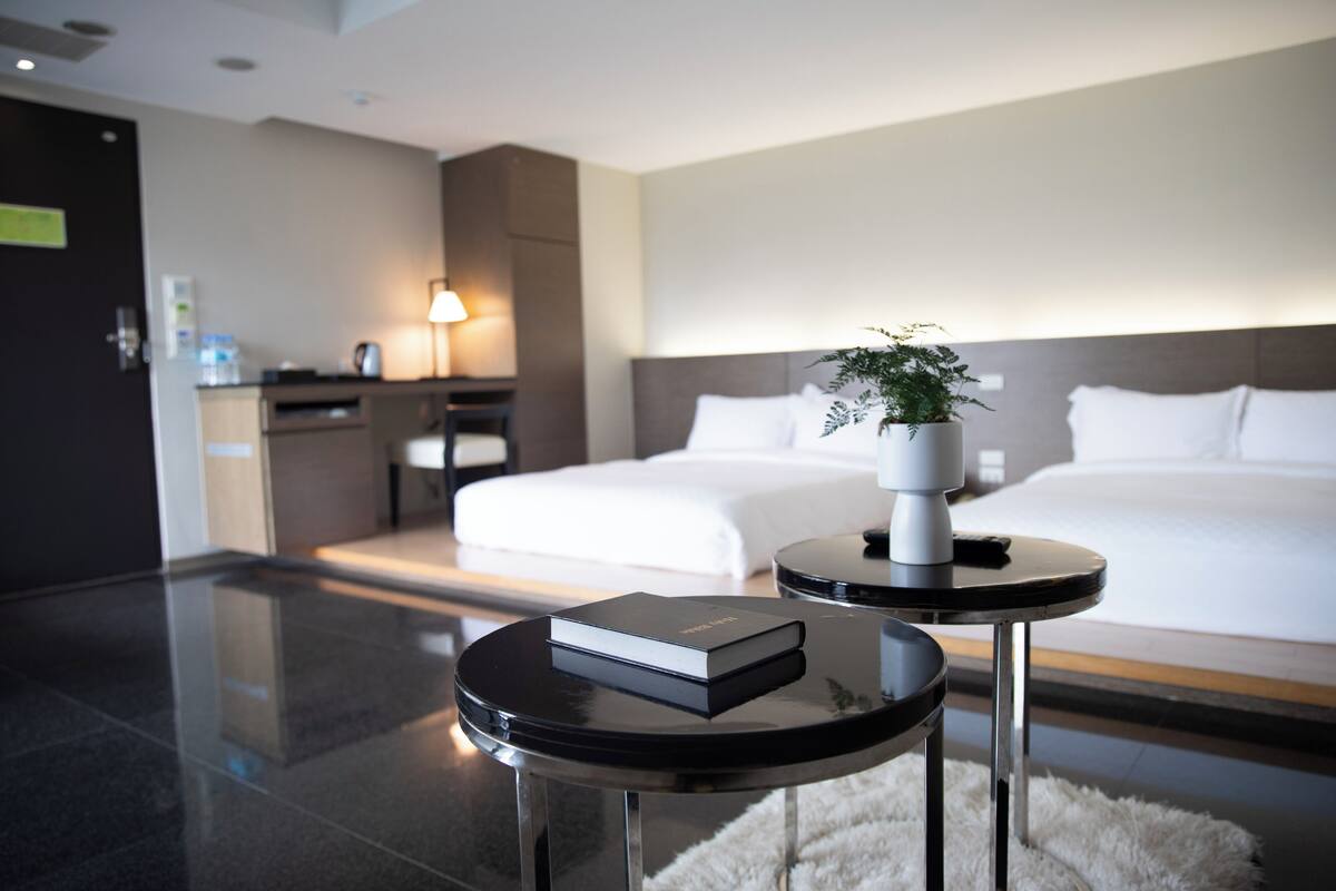 A modern hotel room with a neatly made bed, a bedside table with a book, and a small table with a plant.