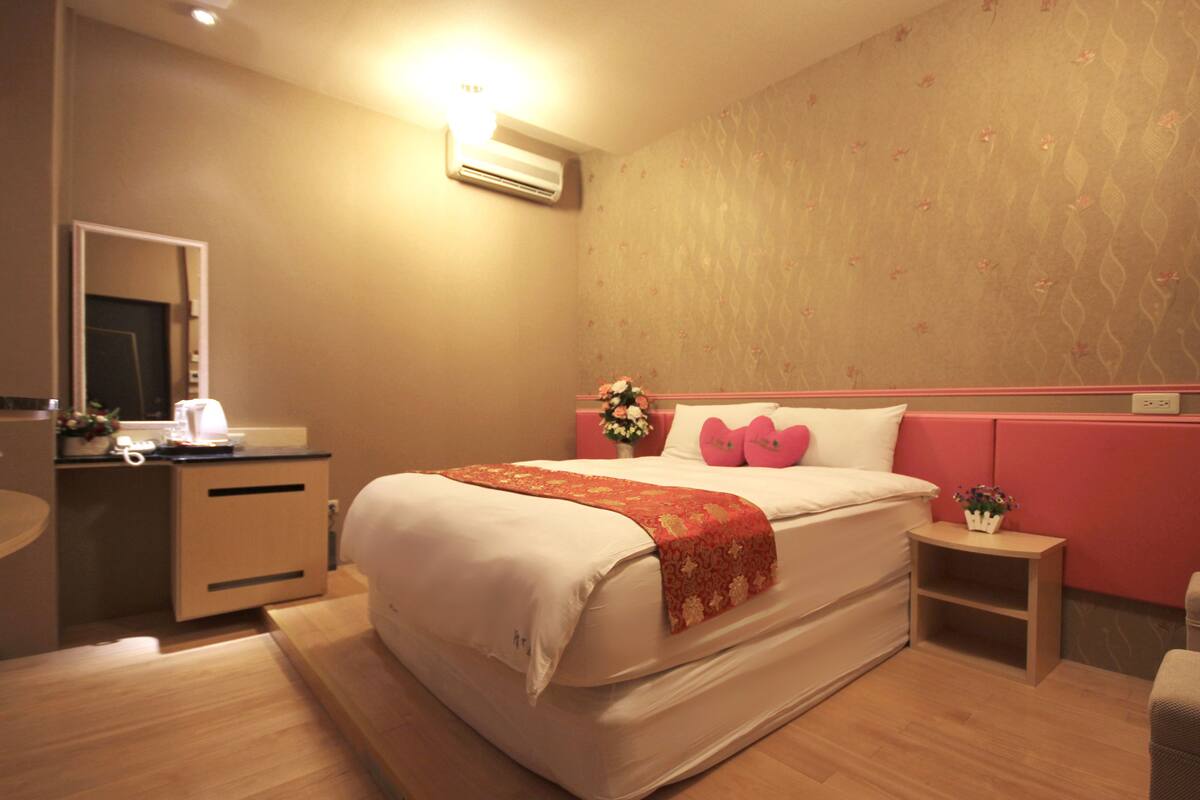 A hotel room with a bed, bedside table, and a mirror.