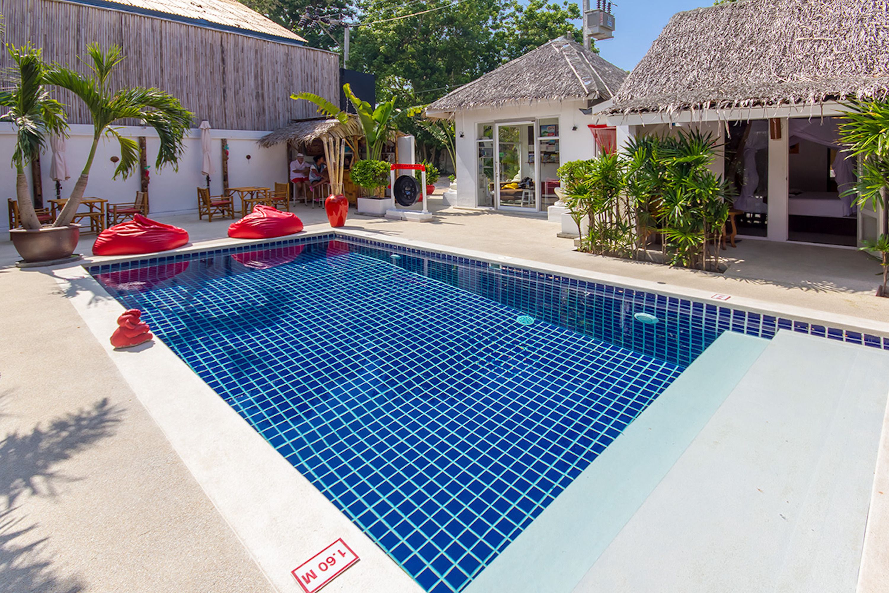 A swimming pool with a tiled edge, surrounded by palm trees and a thatched-roof building.