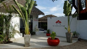 A reception area with a sign for "The White Cottage," a thatched-roof building, and potted plants. - The White Cottage (Koh Samui)