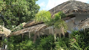 A resort with thatched-roof structures, lush greenery, and a clear sky. - The White Cottage (Koh Samui)