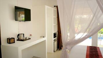 A bedroom with a bed, a TV mounted on the wall, a desk with a coffee maker, and a wardrobe.