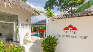 A reception area with a white fence, a statue, and a red potted plant. - The White Cottage (Koh Samui)