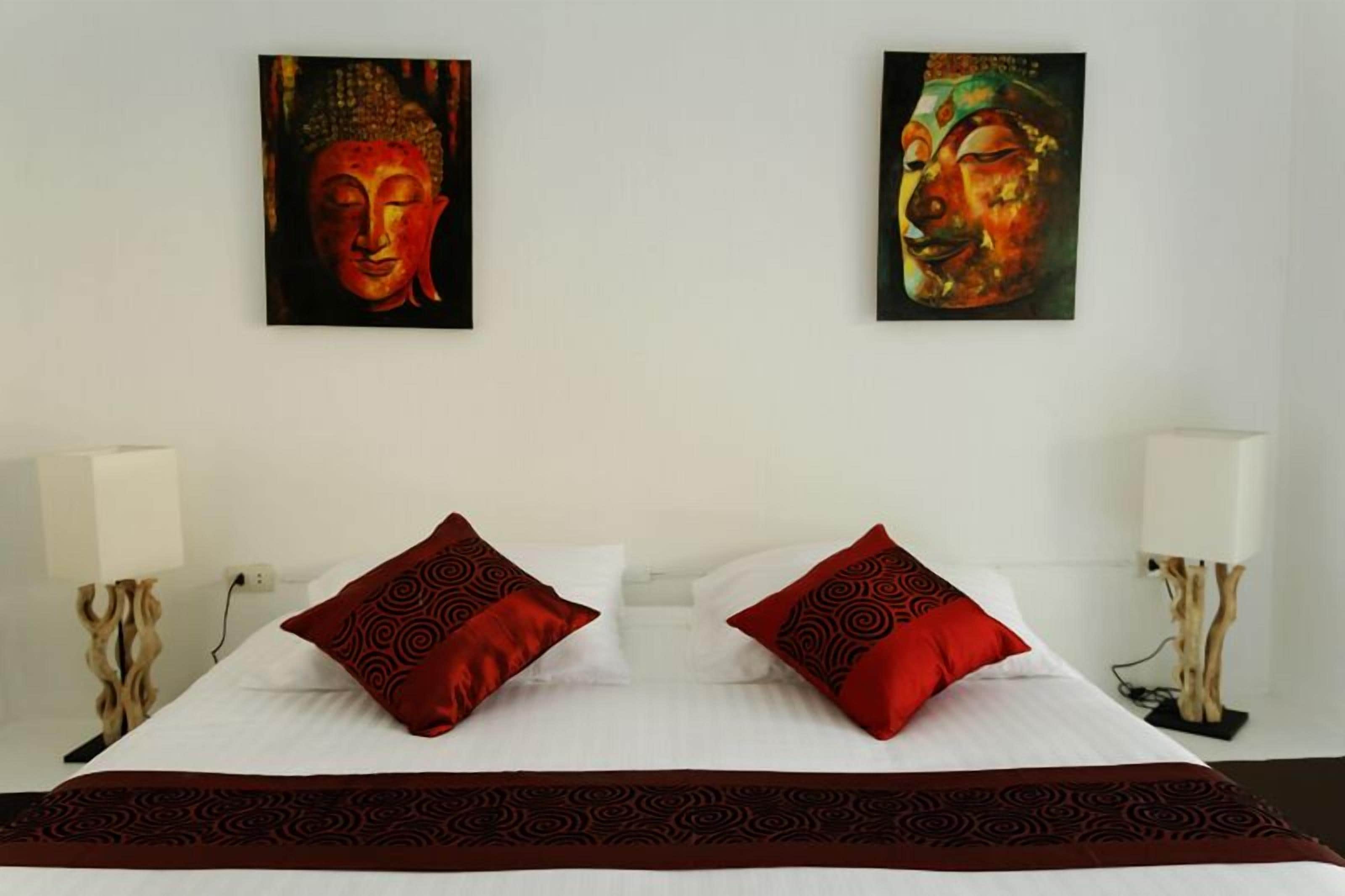 Habitación de hotel con una cama grande, dos almohadas rojas estampadas, dos cuadros colgados en la pared y dos lámparas de noche.