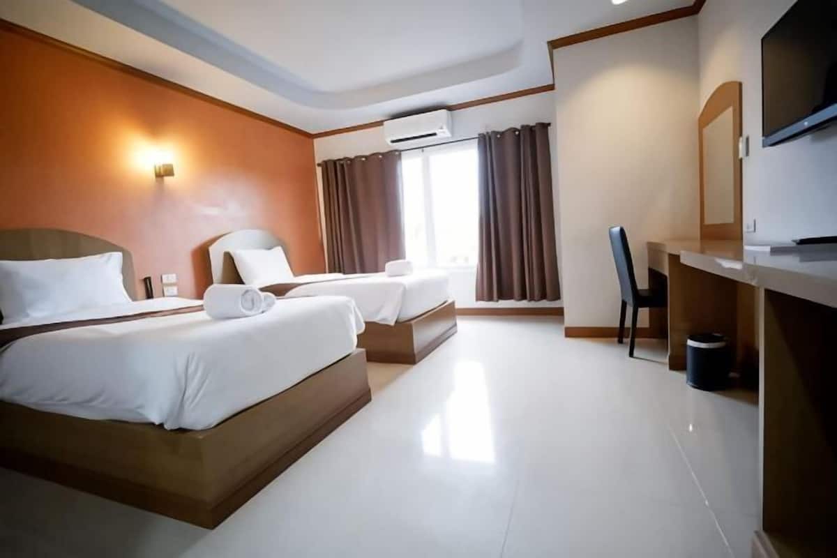 A hotel room with two beds, a desk, a chair, an air conditioning unit, and a television.