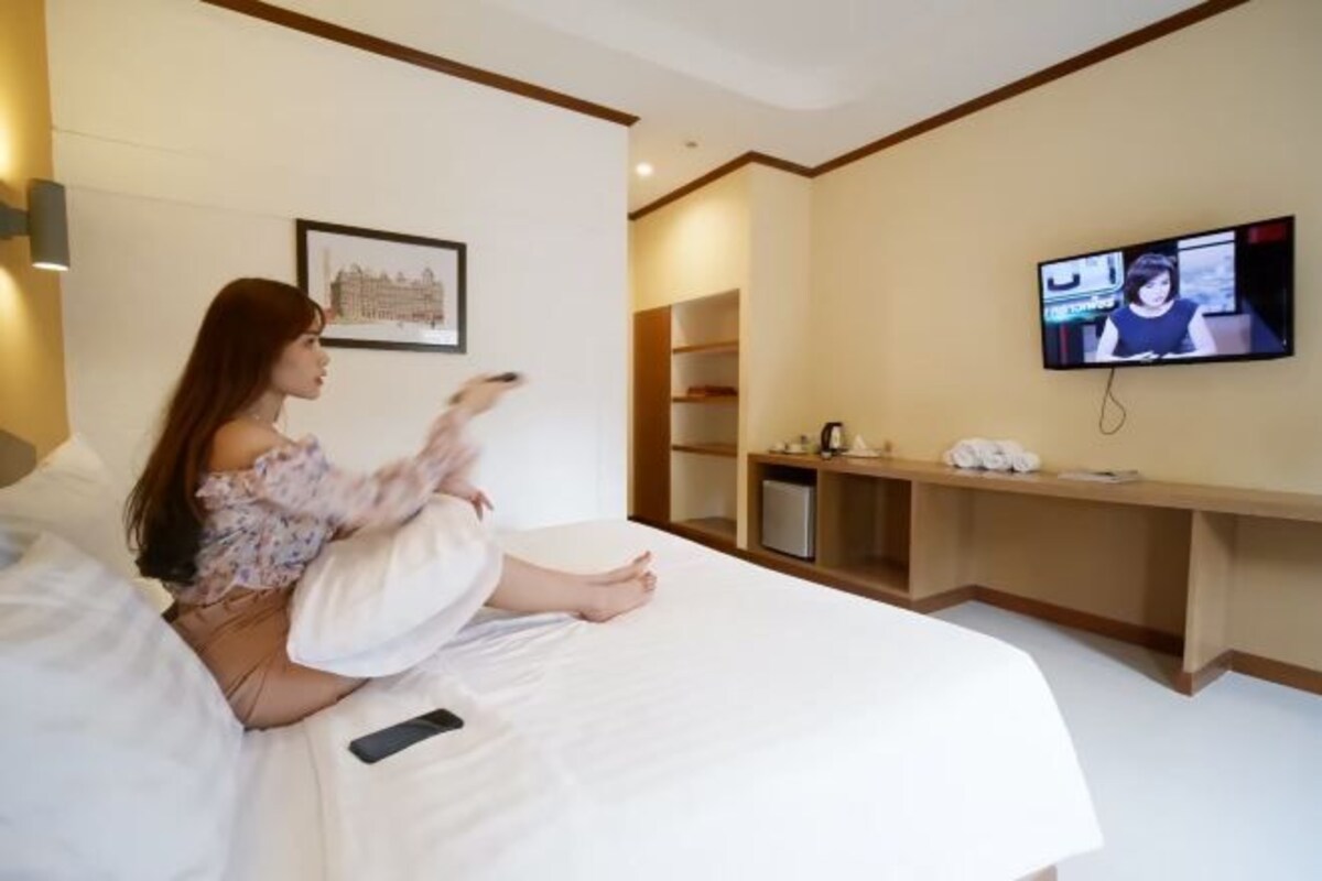 Ein Hotelzimmer mit einem Bett, einem Fernseher, einem gerahmten Bild an der Wand und einem Holzboden mit Gegenständen.