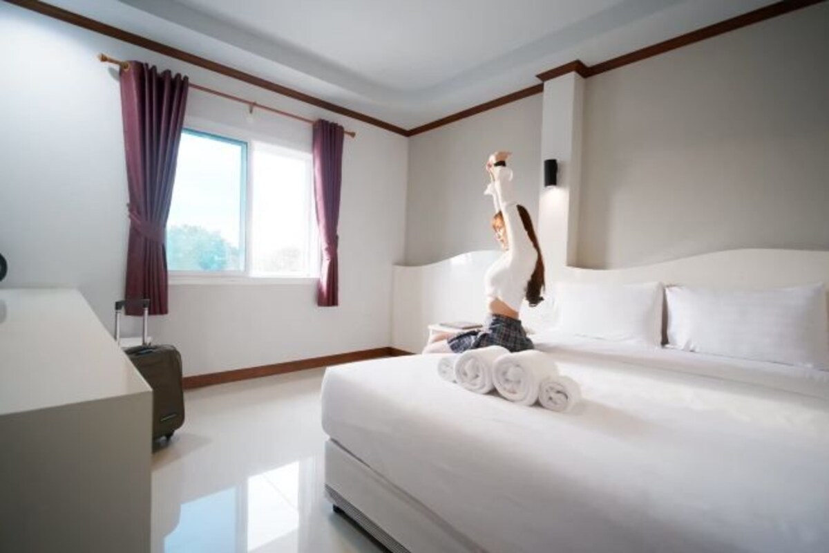 A hotel room with a bed, a desk, a window with curtains, and a suitcase.