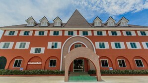 Un hotel a più piani con facciata rossa, persiane bianche e un ingresso centrale ad arco.