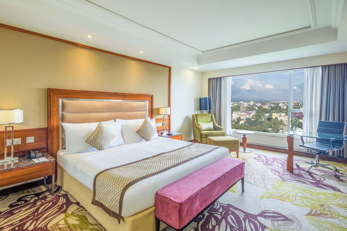 A hotel room with a large bed, a desk, a chair, and a view of a cityscape.