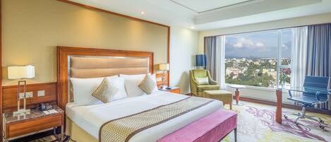 A hotel room with a large bed, a desk, a chair, and a view of a cityscape.