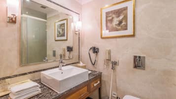Une salle de bain moderne avec un grand miroir, un lavabo blanc, un plan de toilette en marbre et une œuvre d’art encadrée accrochée au mur.