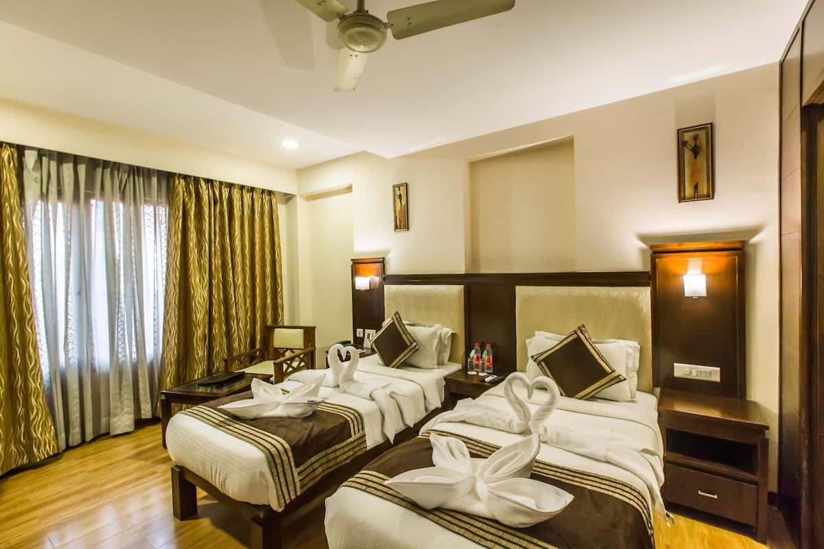 A hotel room with two beds, a ceiling fan, a nightstand, and a window with curtains.