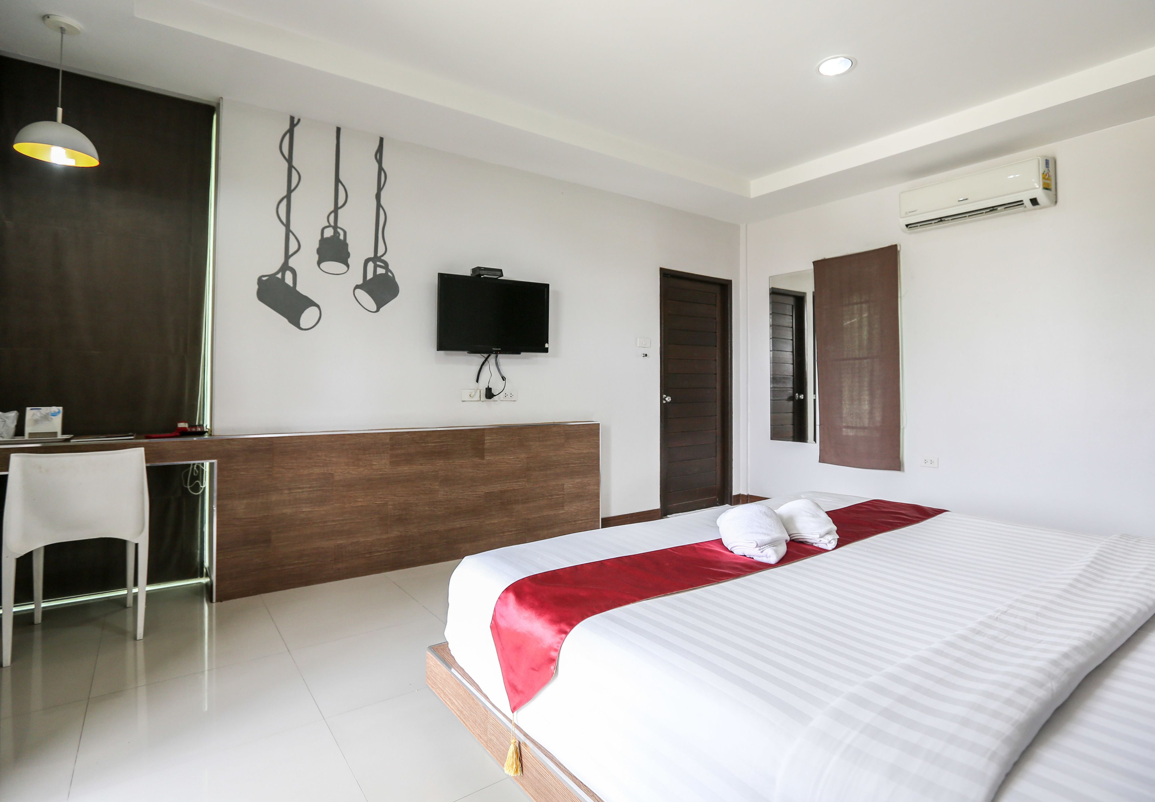 Una habitación de hotel moderna con una cama grande, un escritorio con silla, un televisor de pantalla plana y un equipo de aire acondicionado.