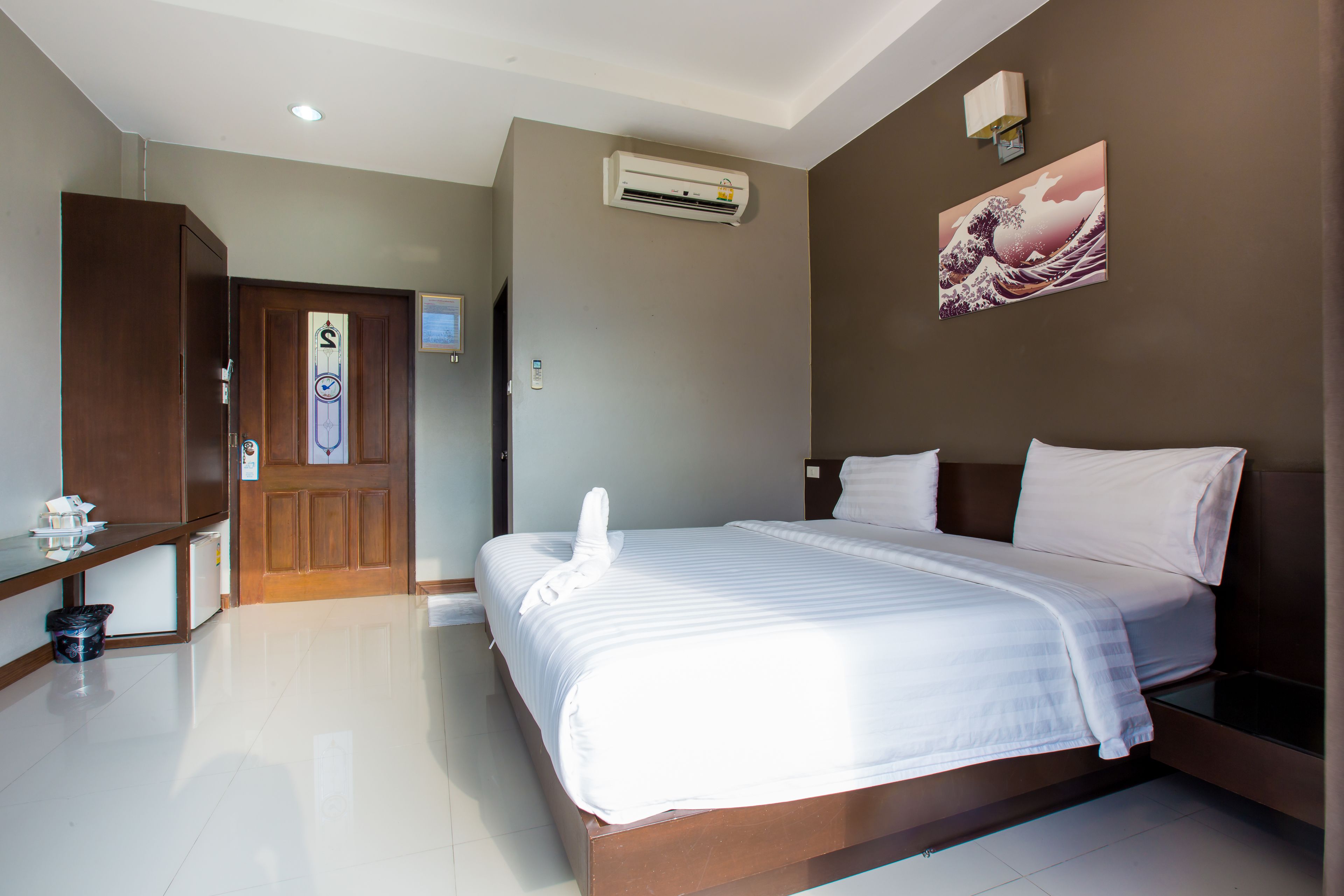 Habitación de hotel con cama, armario de madera, aire acondicionado montado en la pared, un cuadro y una puerta con un cartel.