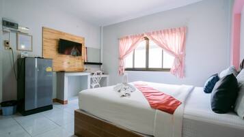 Habitación de hotel con cama, televisor montado en un panel de madera, refrigerador, escritorio y ventana con cortinas.