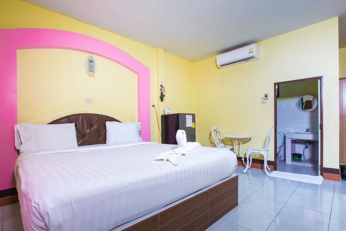 A hotel room with a bed, a small table, a chair, and an air conditioning unit.