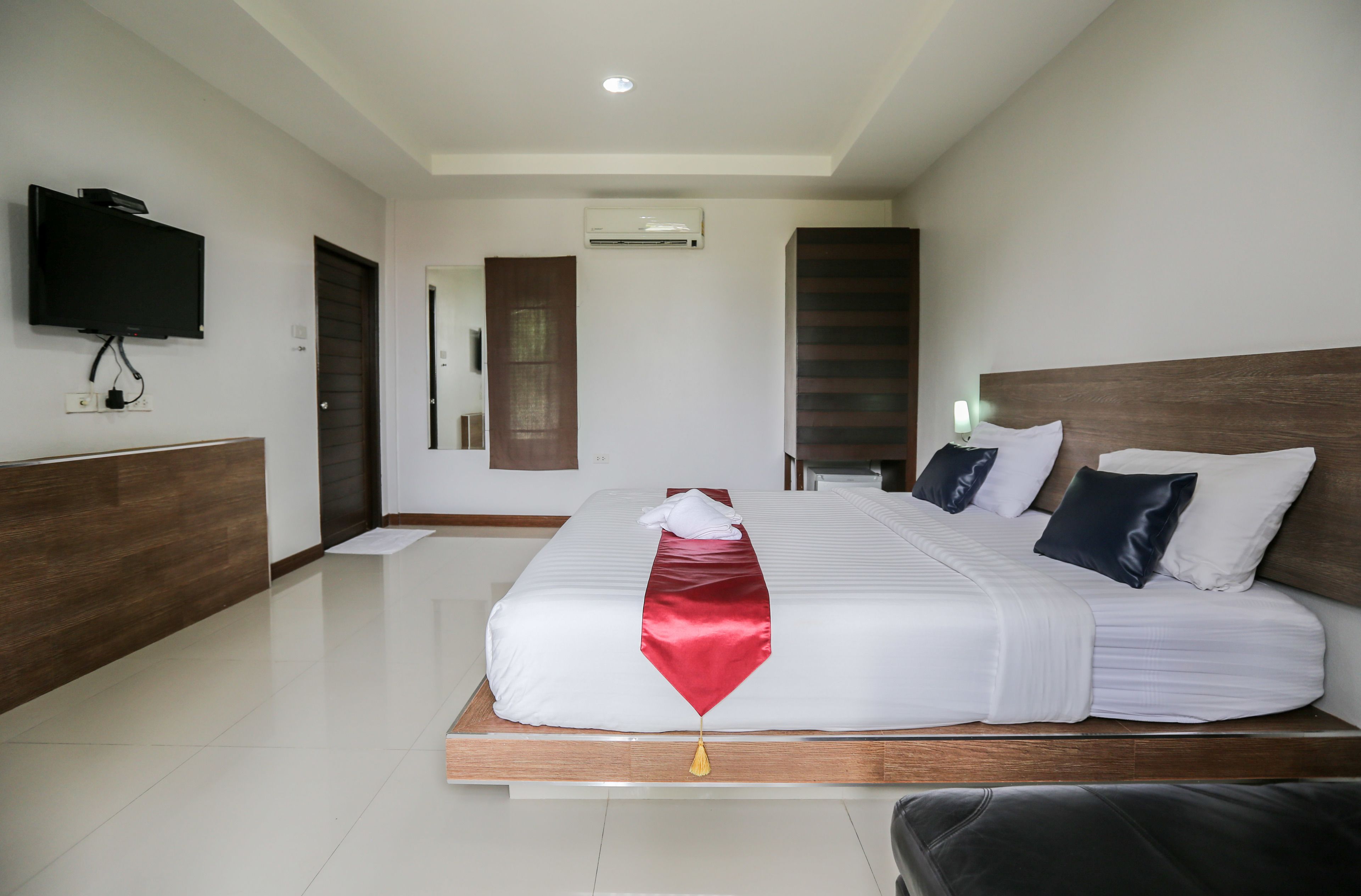 A hotel room with a large bed, a flat-screen TV mounted on the wall, and a wooden headboard.