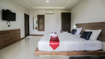 A hotel room with a large bed, a flat-screen TV mounted on the wall, and a wooden headboard.