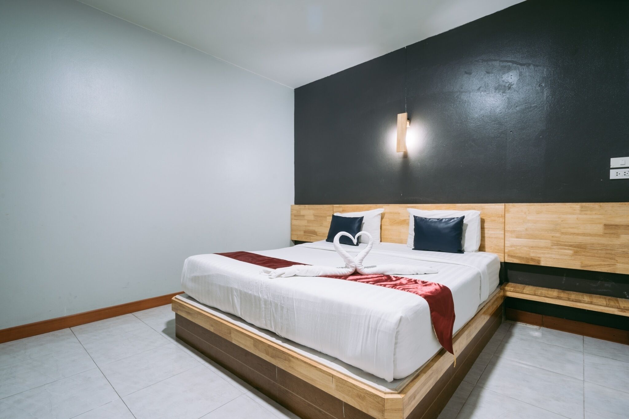 Une chambre d’hôtel avec un lit, une tête de lit en bois, une lampe fixée au mur et une petite table de chevet.