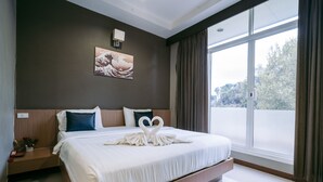 Habitación de hotel moderna con una cama grande, una mesita de noche, una lámpara de pared y un amplio ventanal con cortinas.