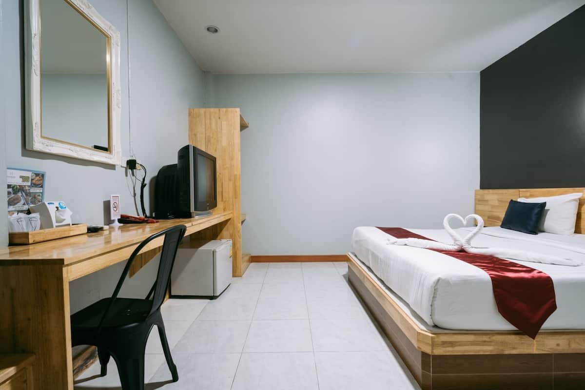 A hotel room with a wooden desk, a television, a bed with white bedding and a red throw, and a mirror on the wall.