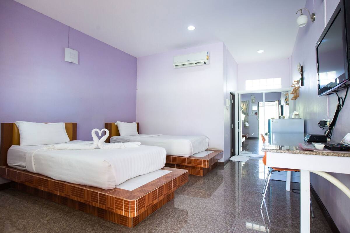 A hotel room with two beds, a desk with a flat-screen TV, and an air conditioning unit on the wall.