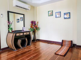 Quarto com piso de madeira, mesa consola com espelho, um vaso com flores e três obras de arte emolduradas na parede.