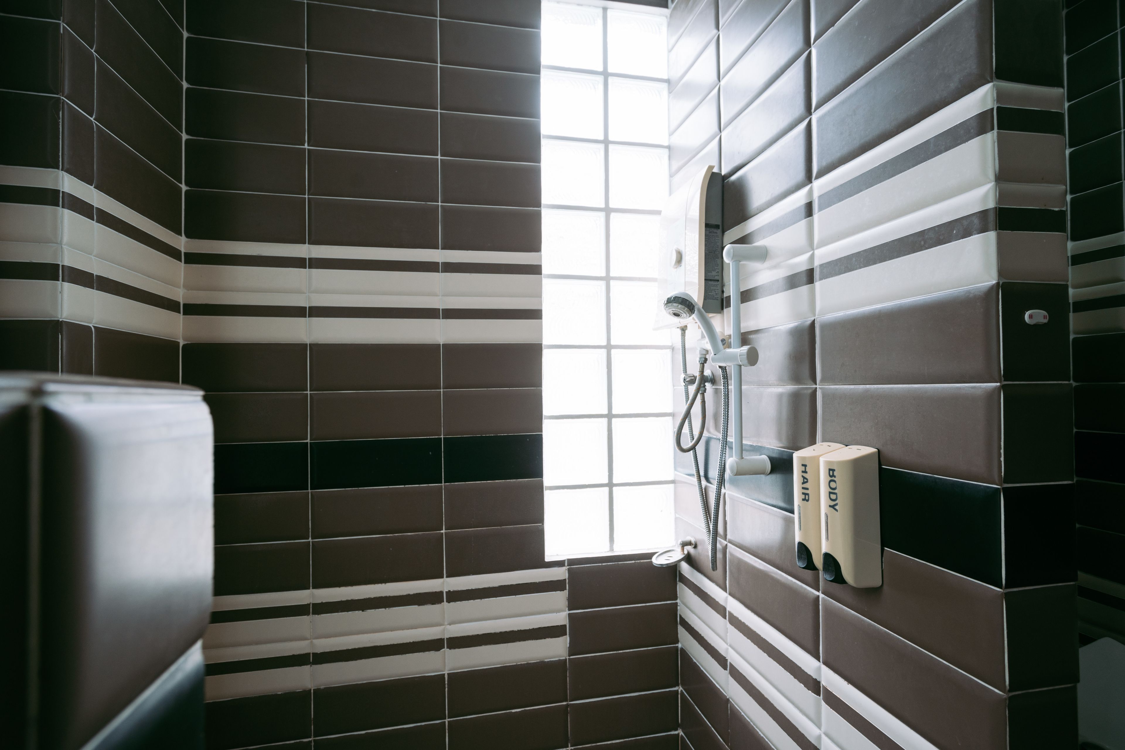 Ein Badezimmer mit gestreifter Fliesenverkleidung, einer Dusche und einem Fenster.