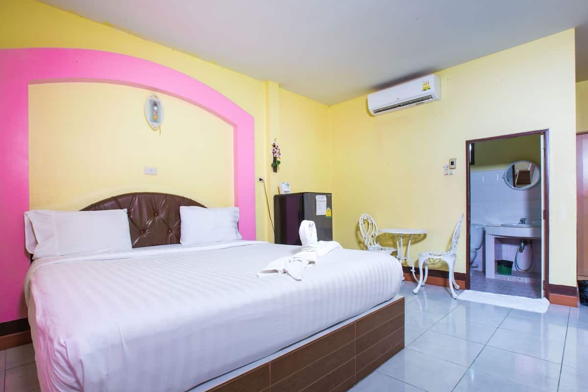 A hotel room with a bed, a small table, a chair, an air conditioning unit, and a bathroom door.