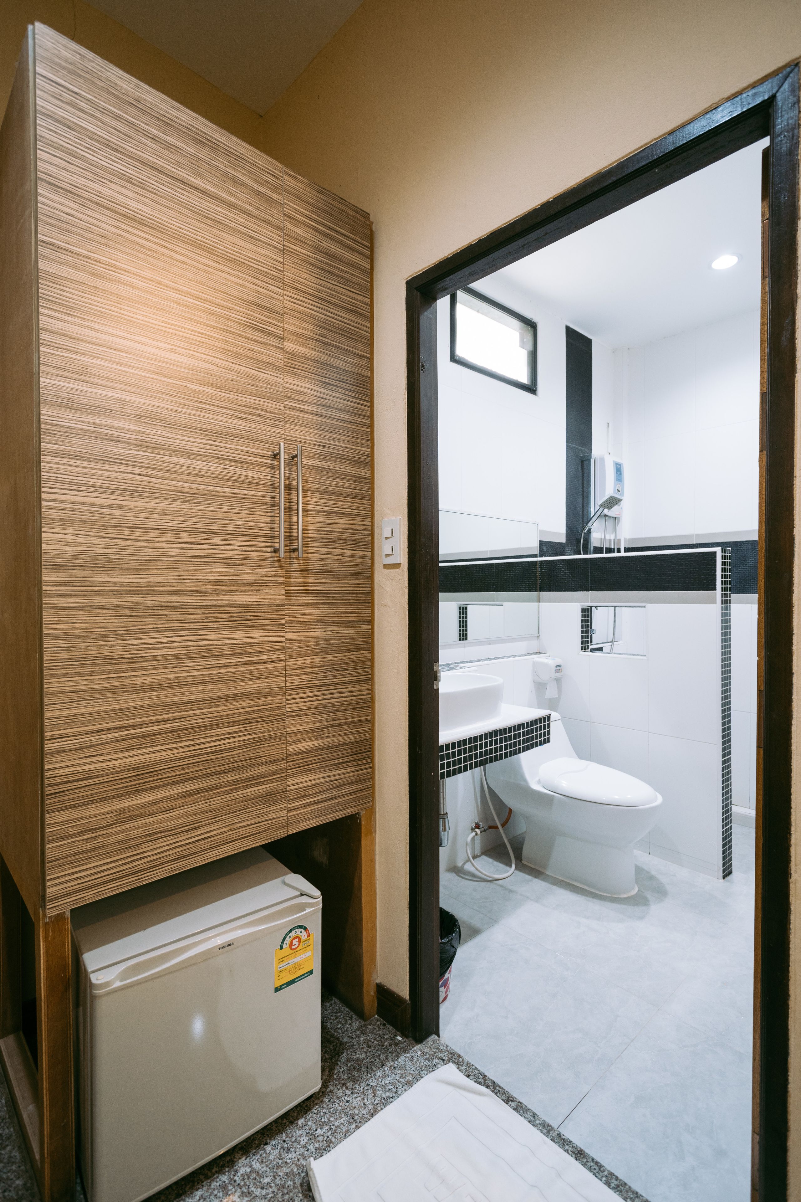 Un baño pequeño con un mueble de madera, un refrigerador compacto, un inodoro y un lavabo.