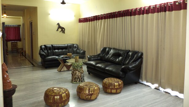 A living room with two black leather sofas, a glass coffee table, and three decorative stools. - Simurg- AK50 New Town (Barasat)