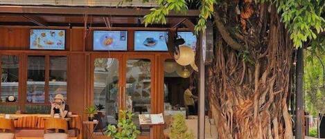 A restaurant with outdoor seating, a large tree, and a traditional wooden facade.