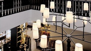 Vestíbulo de hotel de varios niveles con un candelabro central, barandales negros y una exposición de ropa.